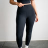Person wearing black athletic leggings and a crop top on a plain background