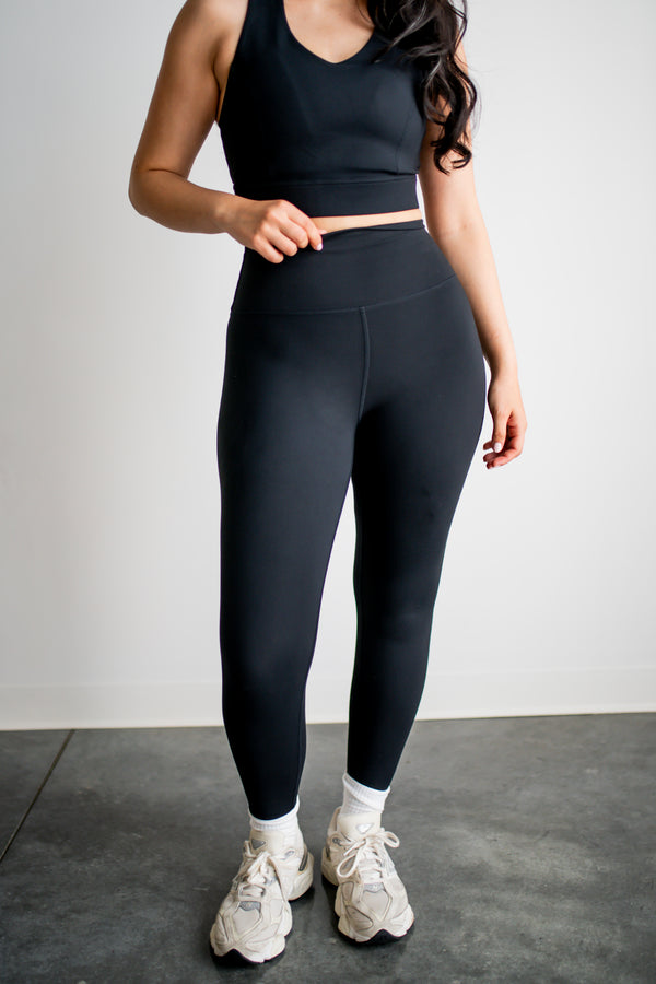 Person wearing black athletic leggings and a crop top on a plain background