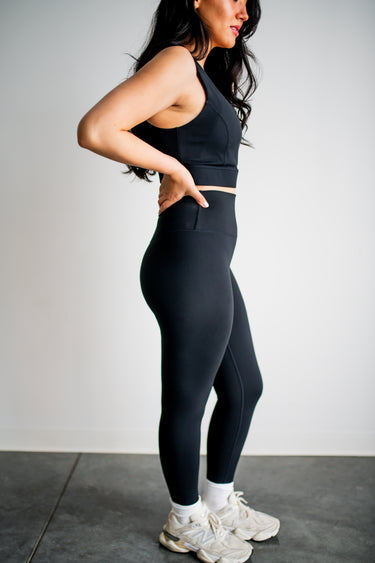 Woman wearing black athletic outfit with white sneakers on a plain background